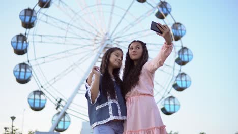 Two-beautiful-girlfriends-make-a-selfie-in-the-background-of-a-Ferris-wheel.-4K