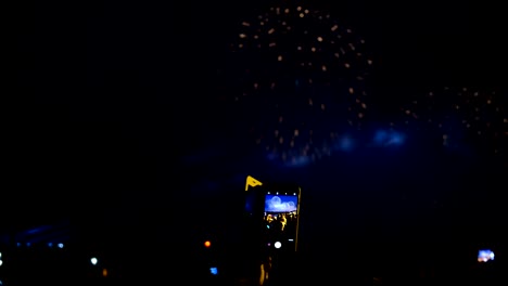 Feuerwerk-und-Masse-durch-den-smartphonebildschirm.-Blick-auf-die-Feuerwerke-und-pyrotechnische-Show-in-den-Abend,-helle-Lichtblitze-Menschen