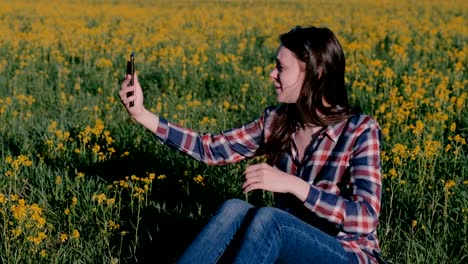 Woman-speak-video-chat-on-the-phone-sitting-on-the-grass-among-the-yellow-flowers.