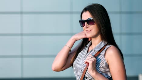 Portrait-of-casual-woman-in-sunglasses-enjoying-sunset-playing-with-her-hair-standing-outdoor