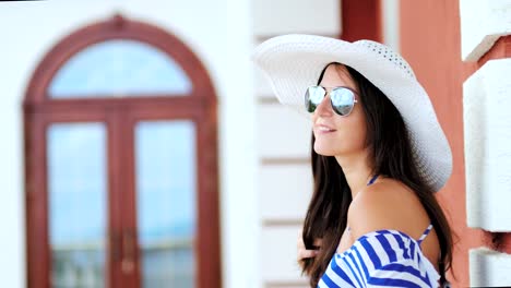 Portrait-of-pretty-young-woman-in-sunglasses-and-hat-playing-with-her-hair-smiling-and-flirting