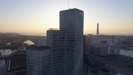 Aerial-4K:-Skyscraper-office-building-in-Malmö-city-at-sunset.-Drone-shot-flying-over-city-and-street-and-backwards,-modern-financial-business-district