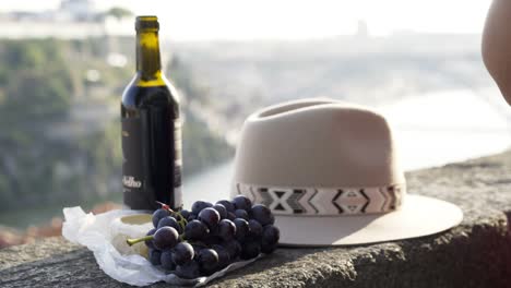 Human-hand-taking-grape-near-bottle-of-drink-and-hat