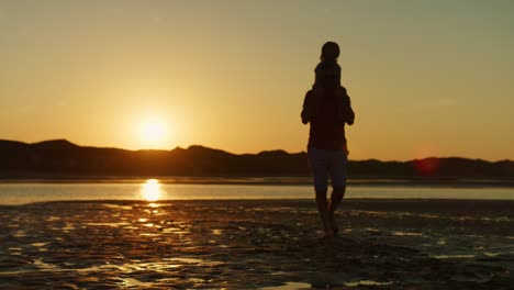 Silueta-del-padre-paseando-con-el-hijo-sobre-sus-hombros-en-la-playa