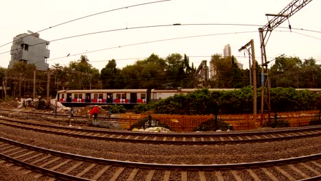 few-people-work-in-distance-on-local-railway-lines-train-goes-behind-background-of-many-storied-houses