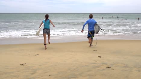 SLOW-MOTION:-Young-surfers-running-into-the-water-carrying-surfboards