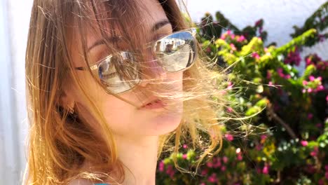 young-girl-with-glasses-stands-near-a-flowering-Bush-smiling-and-blowing-wind