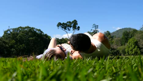 Junges-Paar-am-grünen-Rasen-im-Park-liegen-und-entspannen.-Mann-und-Frau-sitzen-auf-der-Wiese-am-Natur-und-küssen.-Mädchen-und-Jungen-mit-Blick-auf-die-Landschaft-und-Urlaub-genießen.-Geringe-Blickwinkel-hinten-zurück