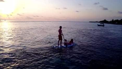 v04106-Aerial-flying-drone-view-of-Maldives-white-sandy-beach-2-people-young-couple-man-woman-paddleboard-rowing-sunset-sunrise-on-sunny-tropical-paradise-island-with-aqua-blue-sky-sea-water-ocean-4k