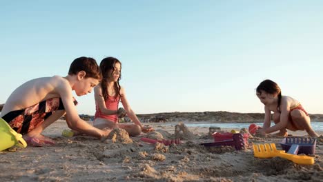 Drei-Kinder-spielen-am-Strand-Sandburgen-zusammen