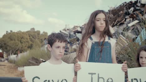 Save-the-planet.-young-kids-holding-signs-standing-inside-a-huge-junkyard