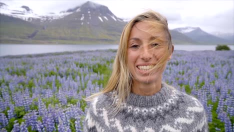 Portrait-von-blonden-Haaren-Frau-in-lupine-Blumenfeld-in-Island-in-der-Nähe-von-See-und-Berge.-Die-Leute-reisen-Glück-Konzept-Zeitlupe