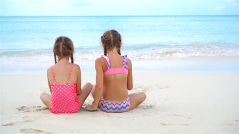 Zwei-kleine-glückliche-Mädchen-haben-eine-Menge-Spaß-am-tropischen-Strand-mit-Sand-spielen