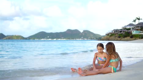 Zwei-kleine-glückliche-Mädchen-haben-eine-Menge-Spaß-am-tropischen-Strand-mit-Sand-spielen