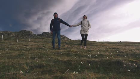 Young-loving-couple-walking-in-field-on-background-of-epic-dramatic-clouds,-slow-motion