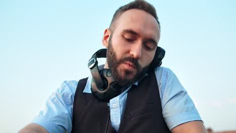 Low-angle-portrait-enthusiastic-happy-male-DJ-in-headphones-at-outdoor-disco-or-rooftop-party