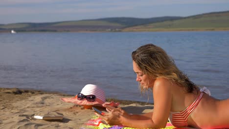 Woman-lie-with-cell-phone-on-the-beach.