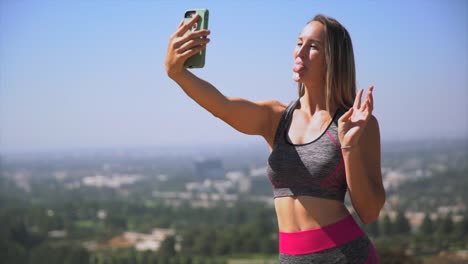 junge-Frau-in-ihre-Trainingskleidung-unter-malerischen-Selfies-mit-ihrem-Handy