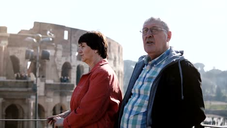 Happy-active-senior-Caucasian-tourist-couple-enjoying-the-view-of-famous-Coliseum-together-during-trip-to-Rome,-Italy.
