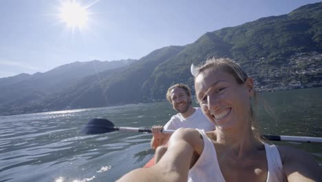 Junges-Paar-in-den-Sommerferien-Kanu-auf-dem-See-in-den-Bergen-zu-genießen.-Die-Leute-Reisen-Spaß-Urlaub-Konzept.-Technologie-und-Jugendkultur-nehmen-Selfie---4K