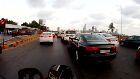 POV-Motorradfahrer-rutscht-durch-Verkehr-auf-der-Straße-in-der-Nähe-von-Meer-weit-Wolkenkratzer-Mumbai