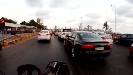 POV-motorcyclist-slips-through-traffic-on-road-near-sea-far-skyscrapers-Mumbai