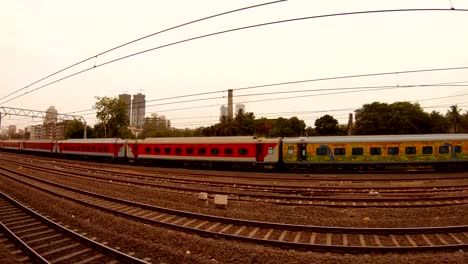 Nahverkehrszüge-bleiben-Zug-mit-roten-Vagonen-weit-Wolkenkratzer-und-grüne-Bäume-Mumbai