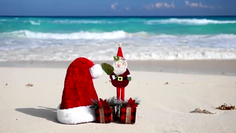 Ayudante-de-Navidad-sombrero-de-Santa-Claus-y-presente-de-juguete-en-la-playa-del-caribe