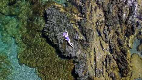 A-woman-in-a-swimsuit-and-hat-lies-on-the-beach.-drone-point-of-view.