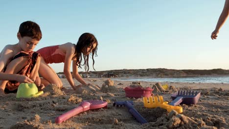 Drei-Kinder-spielen-am-Strand-Sandburgen-zusammen