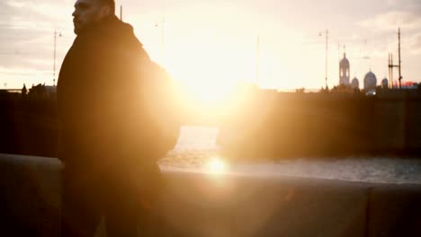 Young-stylish-man-standing-on-embankment-near-river-and-enjoying-the-beautiful-view-on-sunset.-Male-walking-in-evening