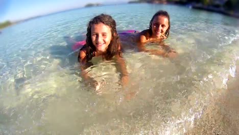 Smiling-little-girls-laying-in-water-on-the-beach