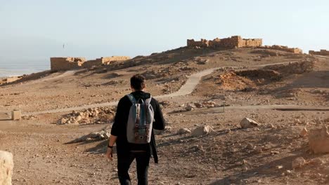 Man-with-backpack-explores-ancient-ruins.-Relaxed-Caucasian-male-tourist-walks-on-summer-desert-rocks-and-sand-Israel-4K