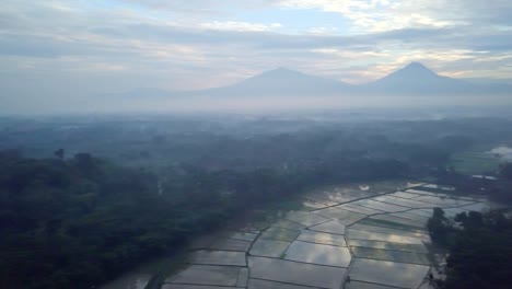 Tiro-de-drone-de-vista-aérea-de-la-ciudad-de-Borobudur-en-Java-en-sunrise,-viajes-Indonesia-religión-drone-concepto-4K-de-resolución-arrozales-y-volcán