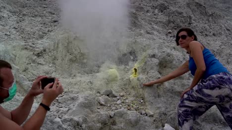 A-man-is-taking-pictures-of-a-woman-next-to-a-fumarole-on-a-smartphone