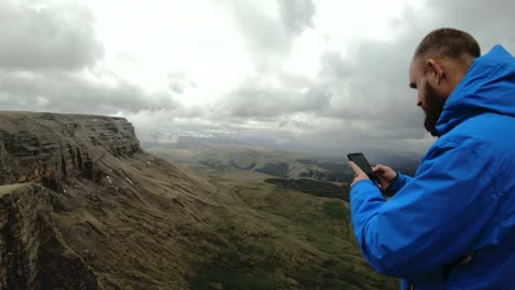 bearded-hipster-man-takes-pictures-on-his-smartphone-while-on-the-rocks-in-the-mountains-of-the-Caucasus