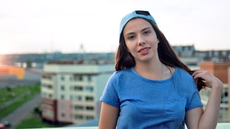 Portrait-of-attractive-smiling-young-teenager-woman-in-cap-touching-her-hair-outdoor