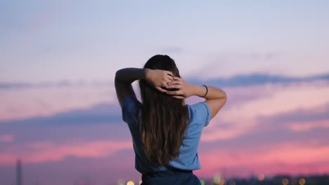 Rear-view-of-young-woman-raising-arms-in-the-air-relaxing-and-enjoying-view-of-wonderful-scarlet-sky