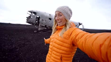 4K-junge-Frau-durch-Flugzeug-Wrack-am-schwarzen-Sandstrand-unter-einen-Selfie-Porträt-berühmten-Platz-stehen-zu-Besuch-in-Island-und-ist-mit-dem-Wrack