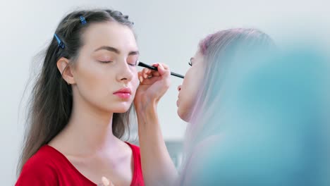 Professional-make-up-artist-putting-light-primer-for-eyelid-of-young-European-woman-client