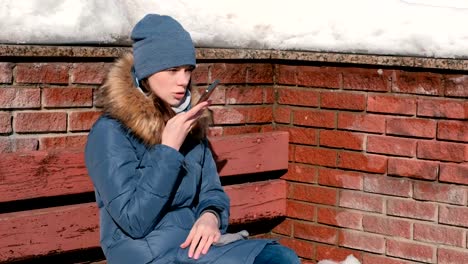 Woman-is-speaking-audio-message-on-mobile-phone-sitting-in-winter-park.