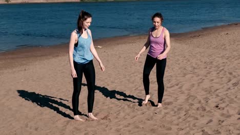 Two-woman-doing-stretching-after-jogging-along-the-sandy-beach-of-the-river-at-sunset.