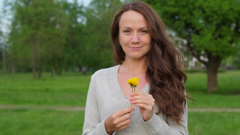 Frau-mit-kleinen-Löwenzahn-in-Händen-in-Landschaft