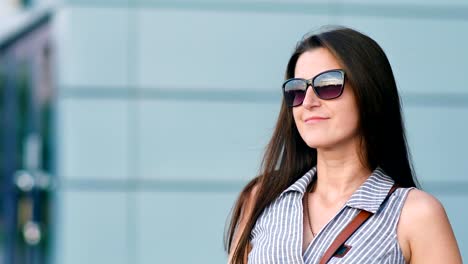 Lovely-woman-standing-near-modern-building-enjoying-outdoor-raising-hands-and-playing-with-hairs