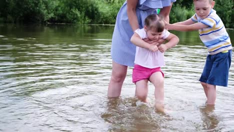 Mutter-des-kleinen-Mädchens-wäscht-seine-Füße-im-Fluss.-Eine-Frau-steht-im-Wasser-mit-ihren-Kindern