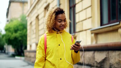 Apuesta-señora-afroamericana-es-escuchando-la-radio-con-auriculares-y-smartphone-moderno,-chica-es-cantando-y-disfrutando-de-música-y-ritmo.