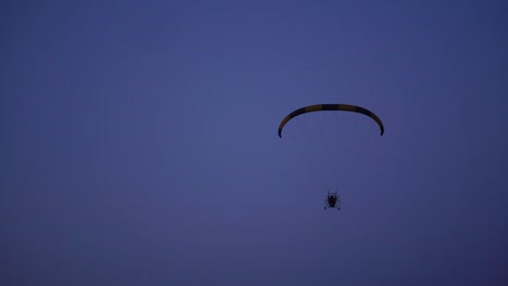 The-pilot-on-a-paraglider-flies-from-the-camera-gradually-moving-away-into-the-distance-against-the-blue-sky