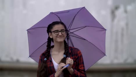 girl-with-an-umbrella-in-the-park-on-a-background-of-a-fountain,-looking-at-the-camera