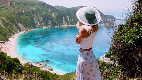 Nette-Frau-mit-Hut,-die-Landschaft-auf-der-griechischen-Insel-zu-bewundern.-Blondine-posiert-vor-atemberaubende-Landschaft-von-Petani-Bucht.-Sommer-Urlaub-Lifestyle-Reisen-Abenteuer-sorglose-Freude-und-Glück-Konzept.-4k-video