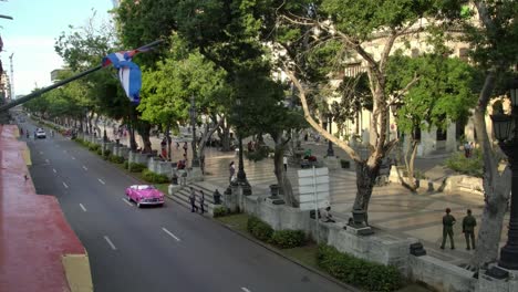 high-angle-establishing-shot-of-classic-convertible-car-on-street-with-cuban-flag-in-Havana,-Cuba